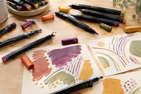 Feutres de dessin Artecho à double pointe disposés sur du papier crème, dans une palette de couleurs variées.