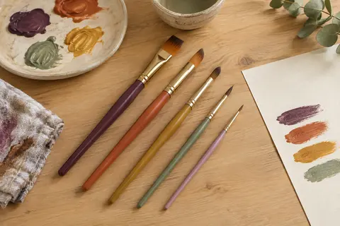 Cinq pinceaux Crayola de tailles différentes, à poils souples, disposés sur une table d’atelier claire.