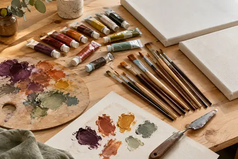 Kit de peinture acrylique avec tubes colorés, pinceaux, palette, spatule et deux toiles sur une table d’atelier