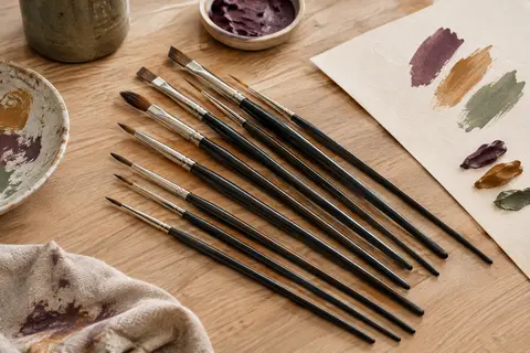 Pinceaux d’artiste à manches noirs et pointes en nylon disposés sur une table d’atelier claire