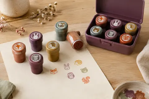 Tampons animaux multicolores rangés dans leur mallette sur une table d’atelier en bois clair