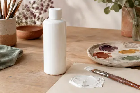 Flacon de gouache liquide blanche posé sur une table d’atelier avec un pinceau et une palette
