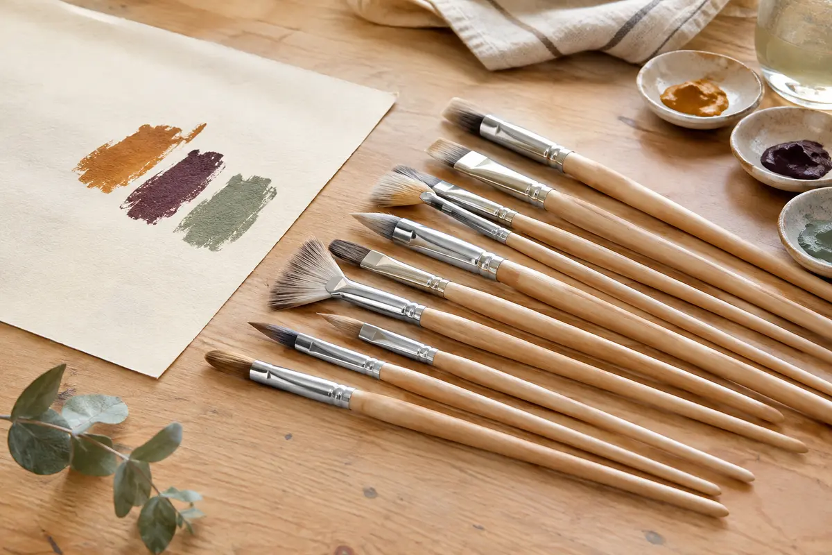 Douze pinceaux en nylon à manches en bouleau et viroles argentées disposés sur une table d’atelier