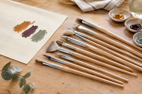 Douze pinceaux en nylon à manches en bouleau et viroles argentées disposés sur une table d’atelier