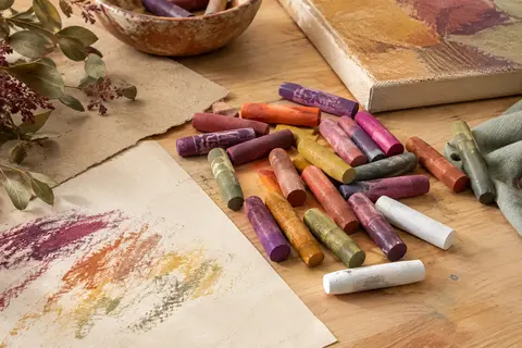 Pastels à l’huile ronds aux couleurs variées disposés sur une table en bois clair près de papier crème.