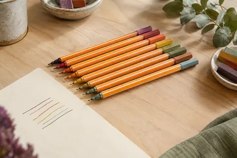 Dix feutres fins orange à rayures blanches disposés sur une table en bois clair avec du papier crème.
