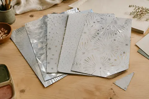 Feuilles A4 de papier cartonné miroir aux motifs argentés disposées sur une table d’atelier en bois clair.