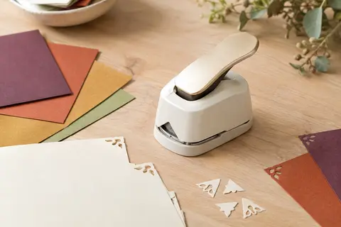 Perforatrice d’angle décorative or blanc posée près de papiers crème découpés sur une table en bois clair