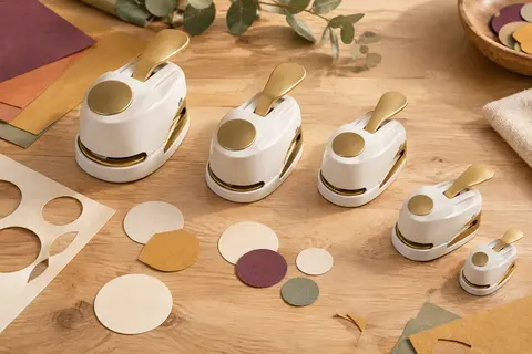 Cinq perforatrices à cercles blanches et dorées avec des découpes de papier sur une table d’atelier en bois clair