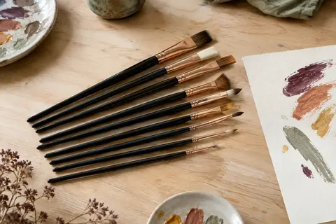 Lot de pinceaux de peinture noirs en nylon, disposés sur une table claire avec du papier et des touches de couleur.