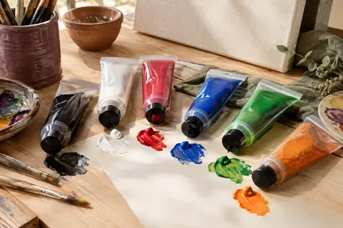 Tubes de peinture acrylique aux couleurs variées disposés sur une table d’atelier en bois clair.